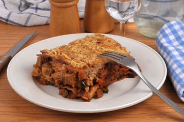 Part de lasagnes aux l&eacute;gumes maison servie dans une assiette avec une fourchette en gros plan servie &agrave; table avec un verre d'eau
