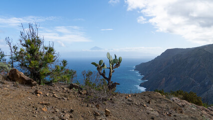 Rauhe Küste mit Klippen auf der Kanareninsel La Gomera, mit dem Vulkan Teide auf Teneriffa im Hintergrund