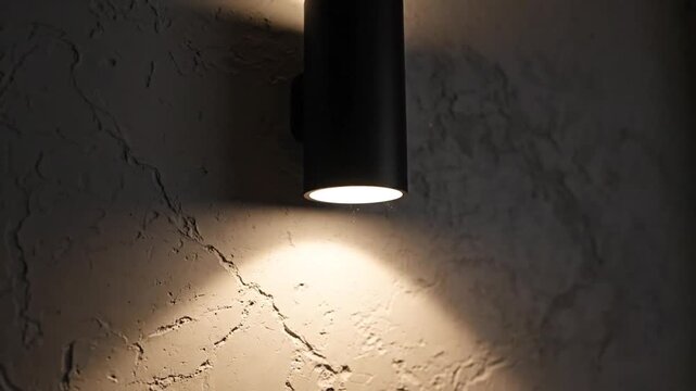 Modern black wall sconce casting soft ambient light onto textured gray wall creating cozy stylish atmosphere with minimalist interior design and contemporary architectural lighting mood