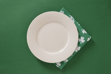 Empty white plate with green napkin on green background for St Patricks day. Clean festive mockup for menu, banner or holiday design.