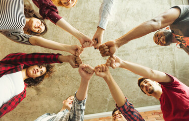 A group of diverse friends is engaging in a fun team-building activity indoors. Their fists are joined together in a circle, symbolizing cooperation and camaraderie among various cultures.
