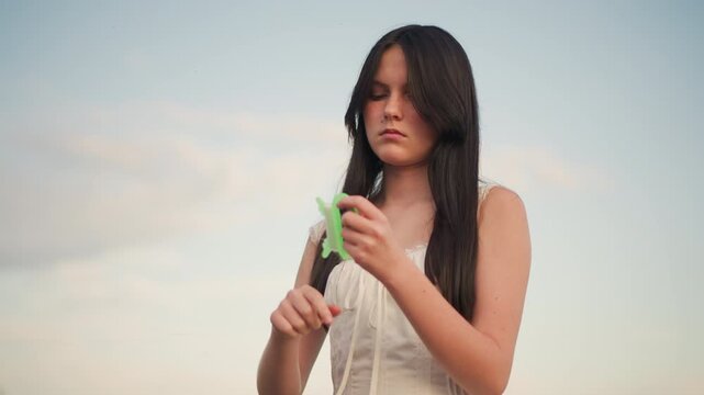 white woman at sunset examining small green device, scrolling and pausing like a traveler and correspondent wide sky backdrop, warm twilight glow, candid closeups of hands and expression,
