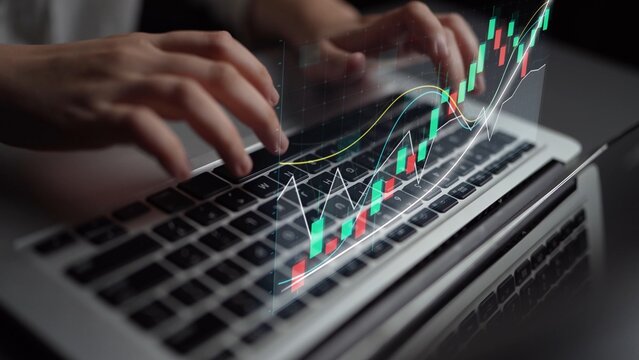 A skilled individual interacts with a laptop keyboard while a digital financial graph displays on the screen, emphasizing the analysis of stock market trends in a contemporary setting. Copula - Powered by Adobe