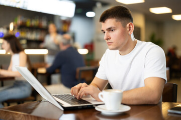 During lunch break, young man spends time with laptop at table in cafe, drinks coffee, and communicates via video link with relatives. Freelance senior woman using laptop and drinks coffee. .