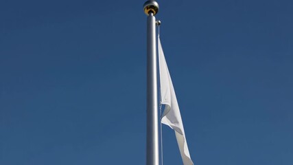 A white flag waves on a tall flagpole set against a backdrop of clear blue sky. the scene conveys themes of peace, surrender, or truce, ideal for concepts related to diplomacy or conflict resolution.