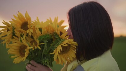 woman holding sunflower bouquet at sunset in open meadow, burying face in petals and inhaling fragrance, rustic florist mood, vibrant yellow blooms and soft dusk glow, joyful intimate gesture