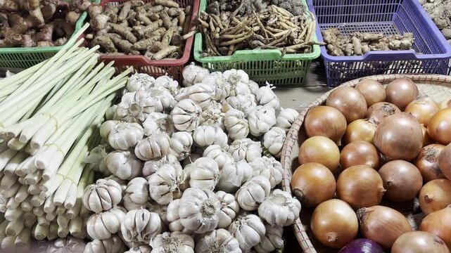 Vibrant fresh market display with abundant white garlic bulbs, green lemongrass stalks, and various onions, showcasing healthy culinary ingredients for cooking