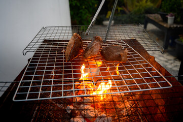 Grilled beef steak on barbecue grill over charcoal fire with tongs. Tender meat sizzling on a barbecue grill with flames below.