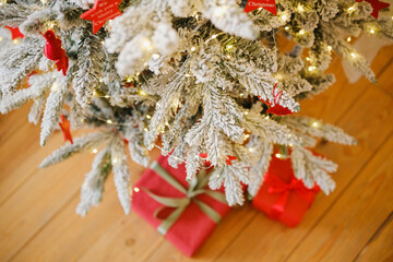 Fototapeta premium Frosted Christmas tree branches with warm lights and red gift boxes below on wooden floor
