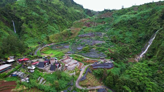 Aerial drone footage of a green small valley in Dieng plateau, Indonesia, called Swiss van Java, with touristic wooden villas and black plantation plastics