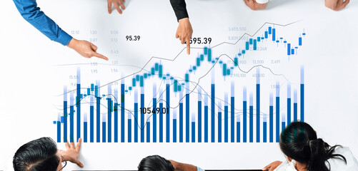 Business professionals analyze financial data on a white table, pointing at charts and graphs, discussing market trends in a collaborative office environment. Scalp