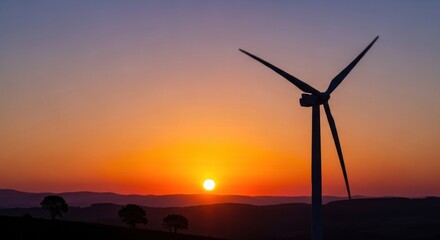 Obraz premium A wind turbine silhouetted against a vibrant sunset sky with mountains in the background.