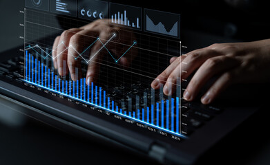 Close-up view of hands typing on a laptop keyboard with digital graphics displaying financial data, trends, and market analysis, illustrating modern workplace technology. Scalp