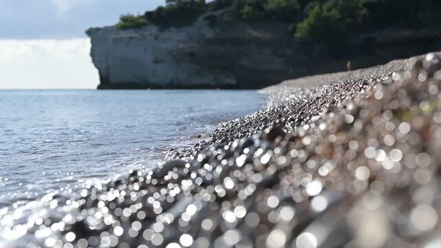 Sunny pebble beach in southern Italy. Gentle waves and sparkling sunlight create a calm mood while a smooth focus shift moves along the shoreline, changing sharpness from near to far stones.