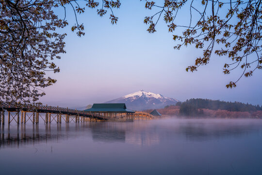 Scenic view of wooden arch Tsuru-no-mai Bridge over Lake with Mountain and Blue Sky during spring cherry blossom season in Aomori Prefecture, Japan