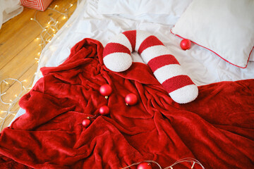 Cozy red blanket with candy cane pillow and ornaments on bed with festive lights