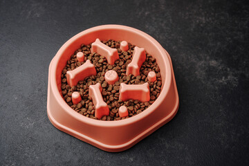 Dog food bowl with bone shapes and kibble on dark surface