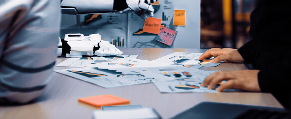 A professional team engages in a business strategy meeting as a robotic arm assists them. They analyze various charts and data, showcasing modern technology in the workspace.Noogenesis