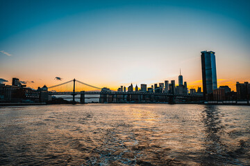 Obraz premium Sunset over Manhattan with the East River view. Beautiful sunset casts vibrant colors over Manhattan's skyline and East River with the bridge in view.