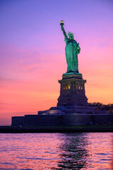 Fototapeta premium Statue of Liberty at sunset with pink sky. Statue of Liberty illuminated by warm sunset colors with a pink and orange sky.