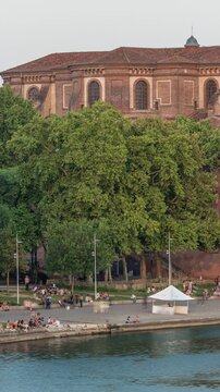Aerial view of Port de la Daurade park along the Garonne River timelapse in Toulouse, France. Sunset orange light, ferry at the dock and people enjoying the vibrant riverside atmosphere
