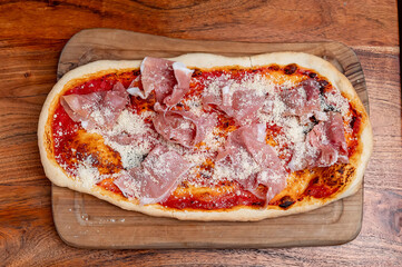 Italian pizza with prosciutto and parmesan on tomato base. Rectangular Italian pizza topped with...
