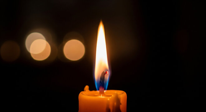 A single lit candle flame in the dark with soft golden bokeh spots in the background - Powered by Adobe