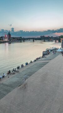 Aerial view of Port de la Daurade park along the Garonne River day to night transition timelapse in Toulouse, France. La Grave Hospital with Saint-Pierre Bridge during sunset with colorful clouds