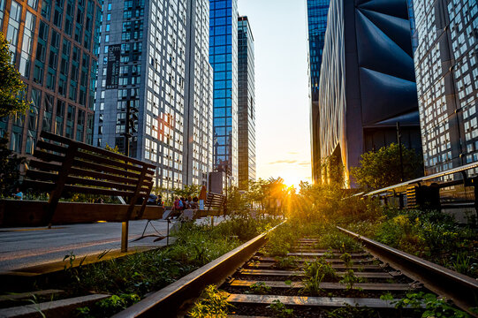 Fototapeta New York, USA, 8 August 2025: Sunlit street seen from above. Evening sun glows between two rows of tall brick buildings