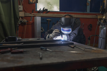 Welder operator wearing personal protective equipment working in the welding workshop, fusing steel parts together, using MIG welding proccess. Metal industry concepts.