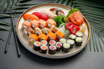 Variety Platter of Sushi, Sashimi, and Maki Rolls. A circular plate features a rich variety of nigiri, sashimi, and maki rolls, showcasing tuna, salmon, eel, and vegetable fillings. © white78