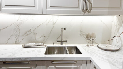 Stylish modern kitchen interior with white marble countertop, double sink, sleek cabinets, under...