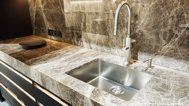 Elegant contemporary kitchen with luxurious dark stone countertop, steel sink, modern faucet, backsplash.