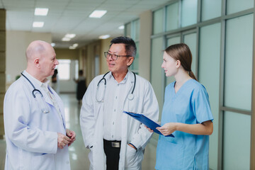 A group of medical professionals, including two doctors in white coats and a nurse in blue scrubs, are standing together in a hospital corridor having a discussion.