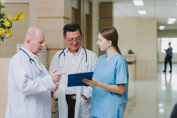 A group of medical professionals, including two doctors in white coats and a nurse in blue scrubs, are standing together in a hospital corridor having a discussion.