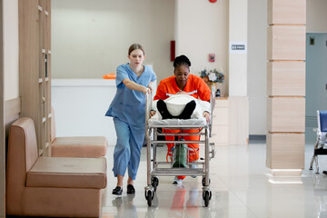 Two nurses, one in blue scrubs and one in orange uniform, rush a patient on a hospital stretcher through the corridor, showing urgency and teamwork in emergency medical care.