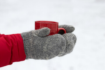 Cup with hot drink in men's hands on winter background.