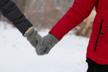 Man and woman in warm clothes holding hands close-up.