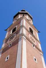 Low-angle view of a historic church clock tower with sundial and pastel facade against a deep blue sky, showcasing traditional European architecture and timeless elegance.