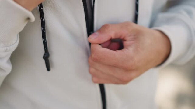 white man adjusting hoodie zipper outdoors with sunlight, closeup sequence of hands pulling cord and aligning fabric, athletic fit showcased for ecommerce and lifestyle, trainer prepping for run then