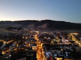 Zakopane - Polska - stolica Polskich Tatr nagrana wieczorem z drona. Swiatła miasta i góry w tle zimową porą podczas zachodu słońca © Konrad