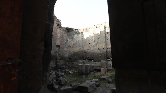  Step through a dark entryway into the majestic interior of an ancient stone ruin, revealing weathered block walls, arched openings, and fragmented windows of historical architecture under daylight.