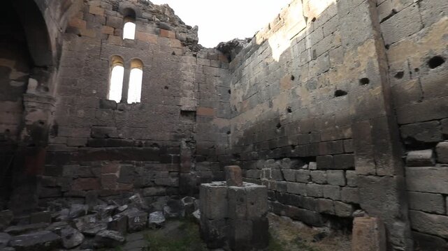  Step through a dark entryway into the majestic interior of an ancient stone ruin, revealing weathered block walls, arched openings, and fragmented windows of historical architecture under daylight.