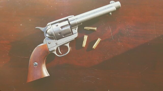 A classic western revolver handgun on a wood table with bullets. Handheld with light leaks and focus pulling.