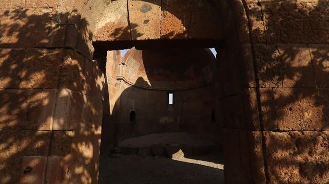  Step through a dark entryway into the majestic interior of an ancient stone ruin, revealing weathered block walls, arched openings, and fragmented windows of historical architecture under daylight.