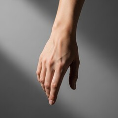 A woman's hand gracefully extended downwards, casting a soft shadow on a neutral grey background, conveying elegance and pause.