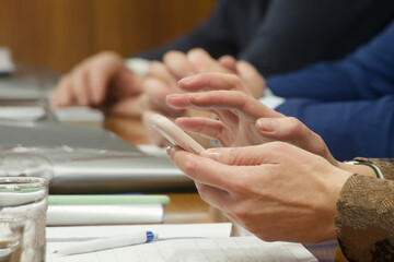 Unrecognizable businesswoman holding a mobile phone during a political congress. Concept of multitasking and digital communication at a corporate negotiation table. Photo