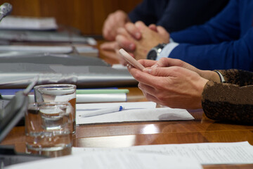 Unrecognizable woman holding a mobile phone during a political congress or board meeting. Concept of distraction and multitasking at work with documents. Photo