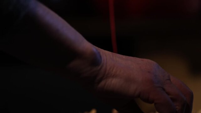 Close-up of hands stringing walnuts on thread for traditional Georgian dessert Churchkhela. Authentic homemade preparation process arranging nuts on a metal tray in a cozy kitchen setting.

