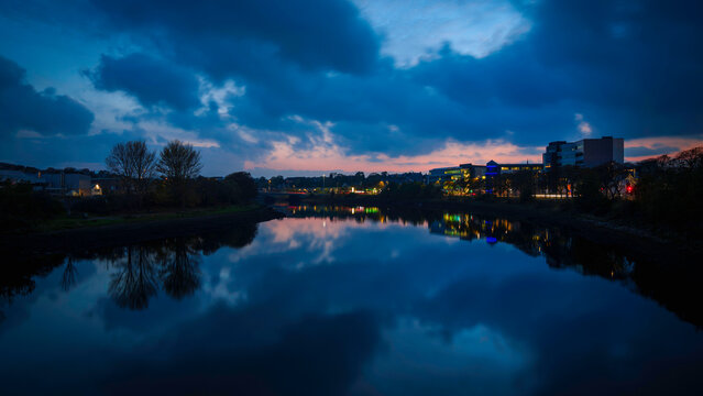 Aberdeen Scotland city night skyline over the River Dee, a view from Victoria Bridge with illuminated buildings and street lights along the riverbank and highway